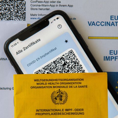 Ein Impfpass und ein Smartphone, auf dem die App CovPass läuft, liegen auf einem Impfzertifikat
