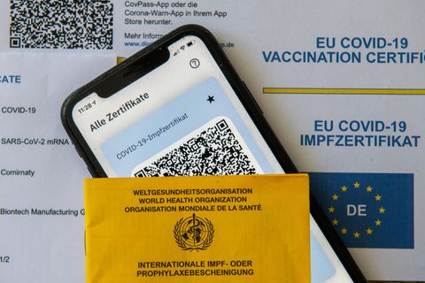 Ein Impfpass und ein Smartphone, auf dem die App CovPass läuft, liegen auf einem Impfzertifikat