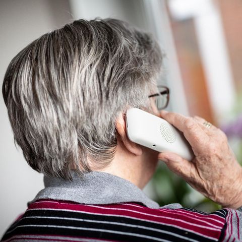 Seniorin telefoniert und schaut dabei aus dem Fenster.