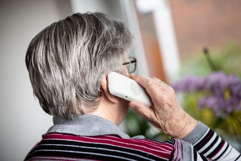 Seniorin telefoniert und schaut dabei aus dem Fenster.