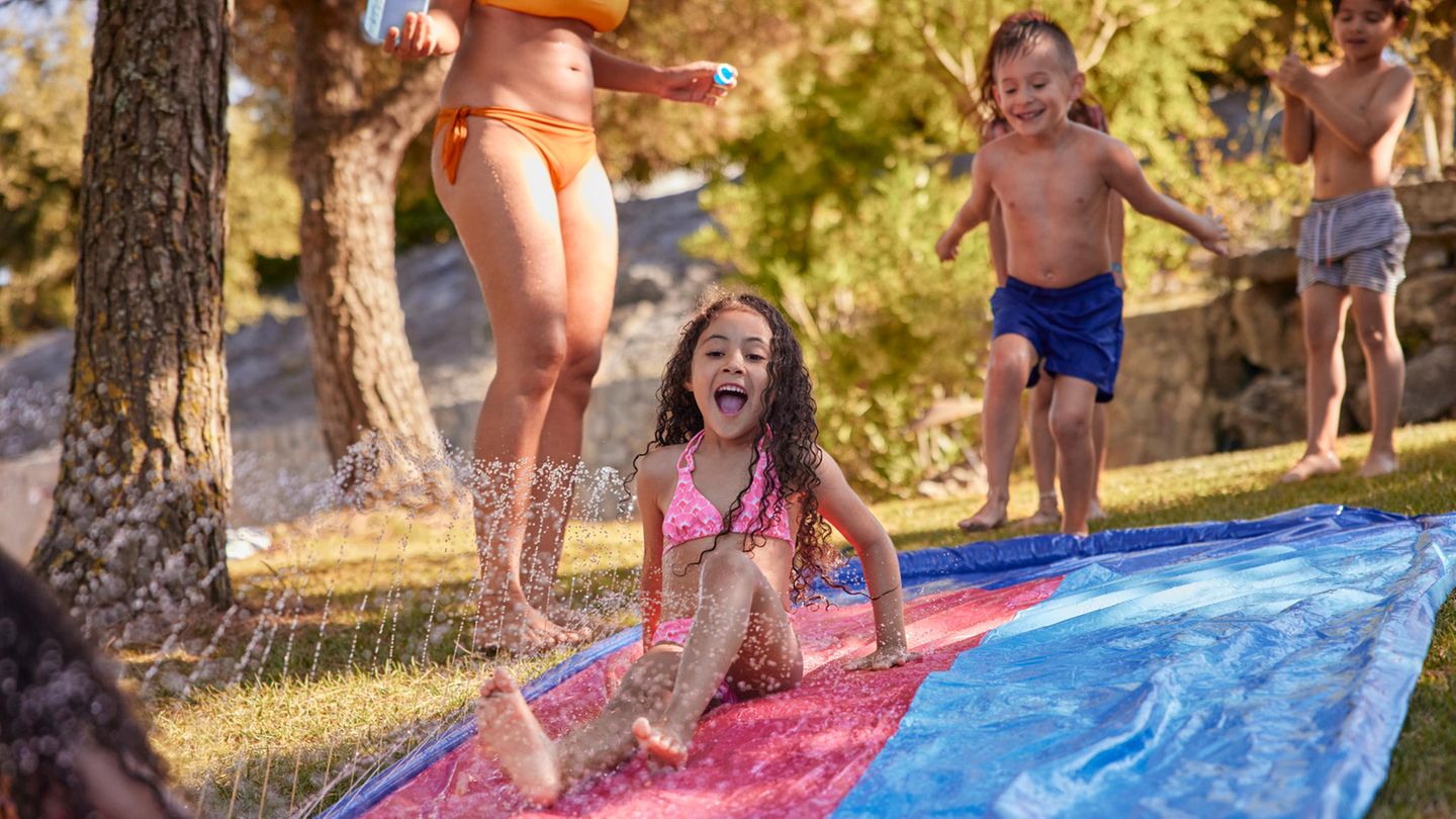 Kindergeburtstag Spiele: Mädchen schliddert im Garten über eine Wasserrutsche