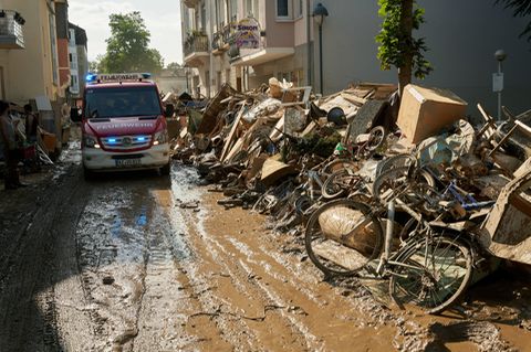 Rheinland-Pfalz, Bad Neuenahr: Ein Einsatzwagen der Feuerwehr fährt durch eine Straße, die mit Sperrmüll gesäumt ist.