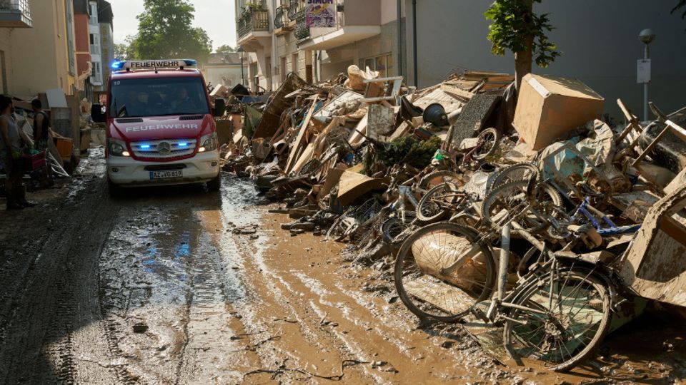 Rheinland-Pfalz, Bad Neuenahr: Ein Einsatzwagen der Feuerwehr fährt durch eine Straße, die mit Sperrmüll gesäumt ist.