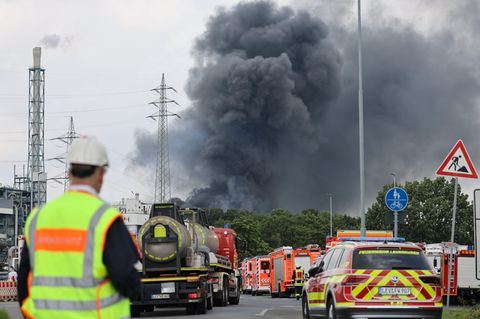 Einsatzfahrzeuge der Feuerwehr stehen unweit einer Zufahrt zum Chempark über dem eine dunkle Rauchwolke aufsteigt