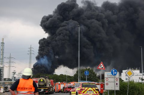 Einsatzfahrzeuge der Feuerwehr stehen unweit einer Zufahrt zum Chempark über dem eine dunkle Rauchwolke aufsteigt