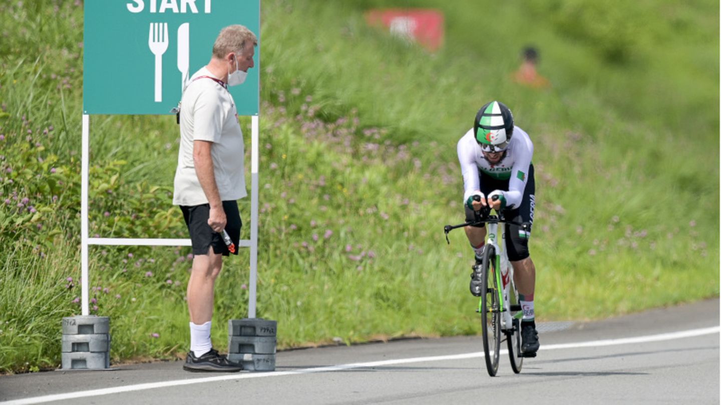 Ein Mann steht am Streckenrand, während ein Rennradfahrer in Montur an ihm vorbeifährt
