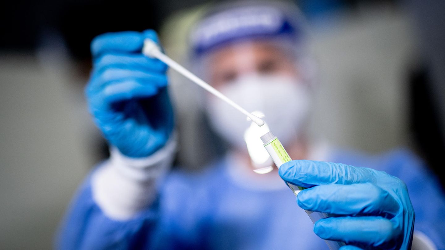 Eine Mitarbeiterin hält eine Probe mit einem Rachenabstrich in die Kamera