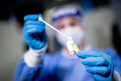 Eine Mitarbeiterin hält eine Probe mit einem Rachenabstrich in die Kamera