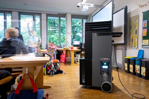 Ein schwarz-grauer Quader auf Rollen und mit Luftschlitzen im oberen Bereich steht in einem Klassenzimmer mit Grundschülern