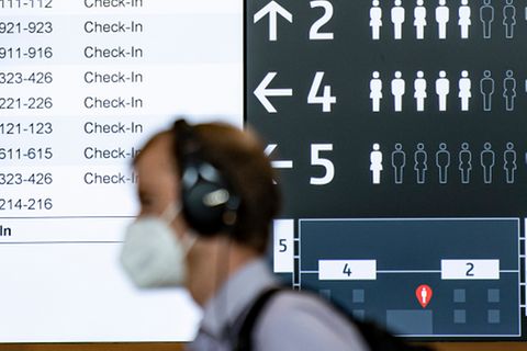 Ein Mann mit Maske geht an einer Anzeigetafel am Flughafen BER vorbei