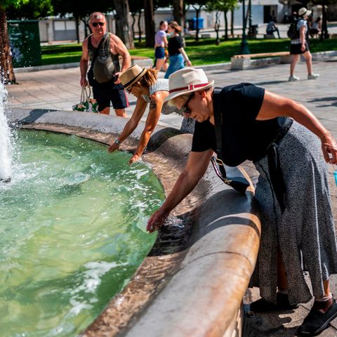 Touristen erfrischen sich bei Temperaturen über 40 Grad mit Wasser aus einem Brunnen auf dem Syntagma-Platz in Athen