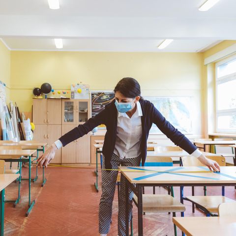 Eine Lehrerin misst den Abstand zwischen den Arbeitsplätzen der Schüler:innen