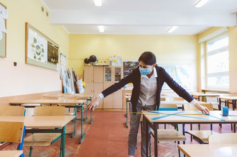 Eine Lehrerin misst den Abstand zwischen den Arbeitsplätzen der Schüler:innen