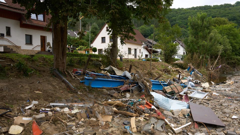 Trümmer liegen an einer Böschung unterhalb einer Wohnstraße, an der zwei weißt Einfamilienhäuser stehen