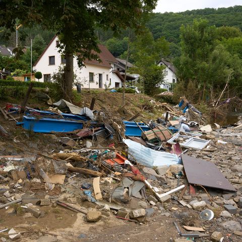 Trümmer liegen an einer Böschung unterhalb einer Wohnstraße, an der zwei weißt Einfamilienhäuser stehen