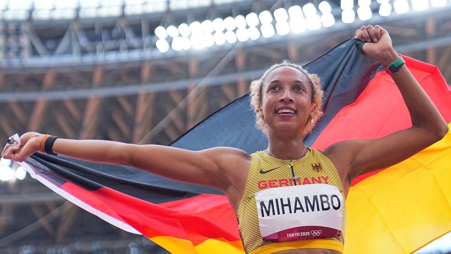 Eine farbige junge Frau im Leichtathletik-Dress und "Mihambo" als Startnummer jubelt mit deutscher Flagge über dem Kopf