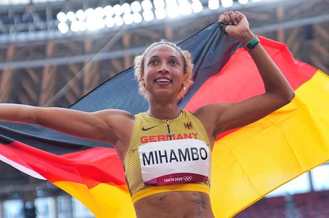 Eine farbige junge Frau im Leichtathletik-Dress und "Mihambo" als Startnummer jubelt mit deutscher Flagge über dem Kopf