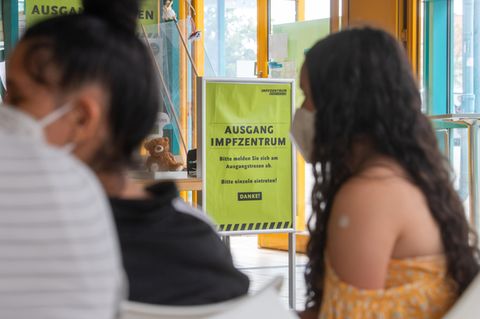 Ein Mädchen mit langen, schwarzen Locken sitzt in gelbem Top und mit einem Pflaster auf dem linken Oberarm im Warteraum