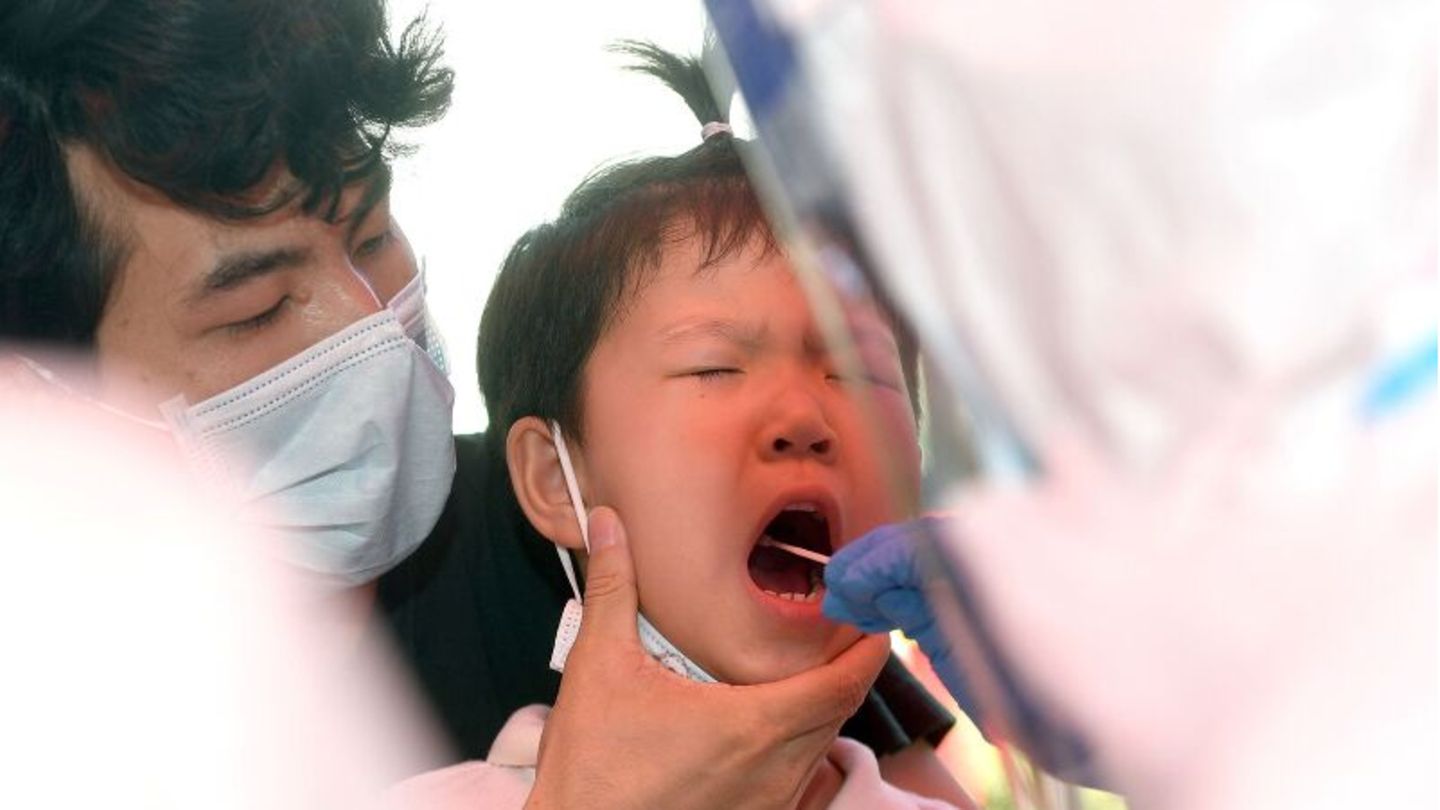 In Wuhan wird ein Kind auf das Coronavirus getestet, ein Erwachsener hält seinen Kopf, ein anderer testet im Rachen