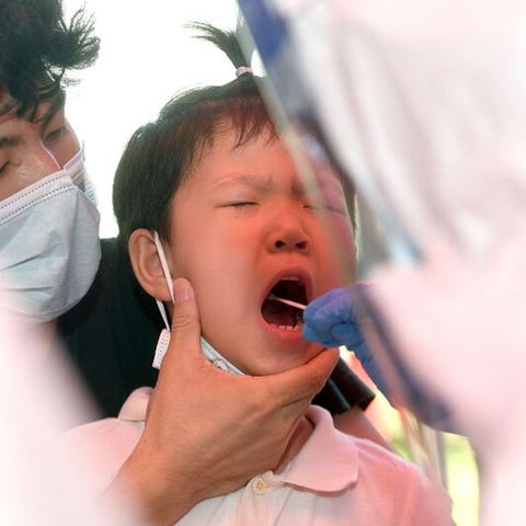 In Wuhan wird ein Kind auf das Coronavirus getestet, ein Erwachsener hält seinen Kopf, ein anderer testet im Rachen