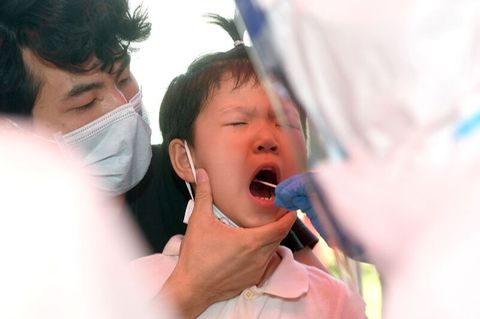In Wuhan wird ein Kind auf das Coronavirus getestet, ein Erwachsener hält seinen Kopf, ein anderer testet im Rachen