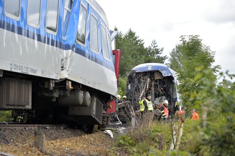 Rettungskräfte in gelben und orangen Warnwesten stehen zwischen einem gestauchten und einem am Ende offenen Zugwaggon