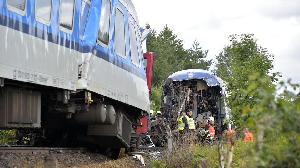 Rettungskräfte in gelben und orangen Warnwesten stehen zwischen einem gestauchten und einem am Ende offenen Zugwaggon