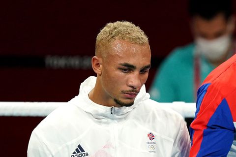 Ein farbiger Mann mit blondierten Locken steht in weißem Trainingsblouson und enttäuschtem Gesichtsausdruck in einem Boxring