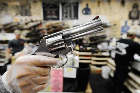Eine rechte, weiße Männerhand in einem durchsichtigen Gummihandschuh hält einen silbernen Revolver mit kurzem Lauf