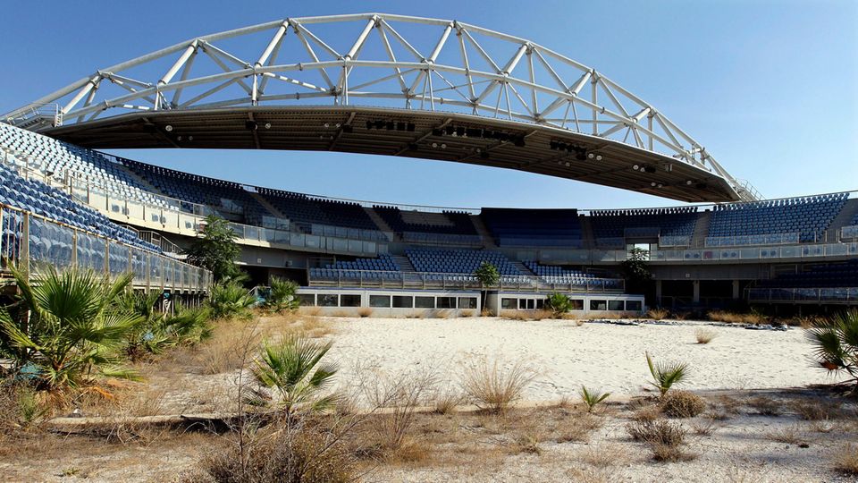 ... glauben, dass die Olympischen Spiele in Athen einer der Faktoren waren, die Griechenland finanziell in die Knie gezwungen haben. Hier zu sehen: die verlassene Beachvolleyball-Arena, aufgenommen zehn Jahre nach den Spielen 2004. Hier holt sich die Natur ihren Lebensraum langsam zurück. 