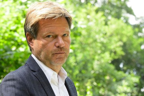 Robert Habeck schaut über seine Schulter in die Kamera - im Hintergrund frisch-grüne Bäume