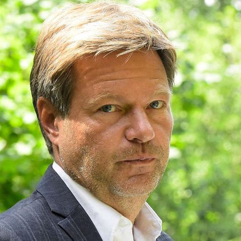 Robert Habeck schaut über seine Schulter in die Kamera - im Hintergrund frisch-grüne Bäume