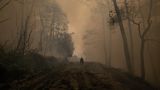 Evia, Griechenland. Ein Mann fährt mit seinem Motorrad durch den Rauch eines Waldbrandes