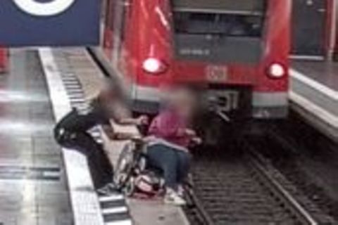 Ein Mann hält eine Rollstuhlfahrerin fest, um den Absturz ins Gleisbett zu verhindern