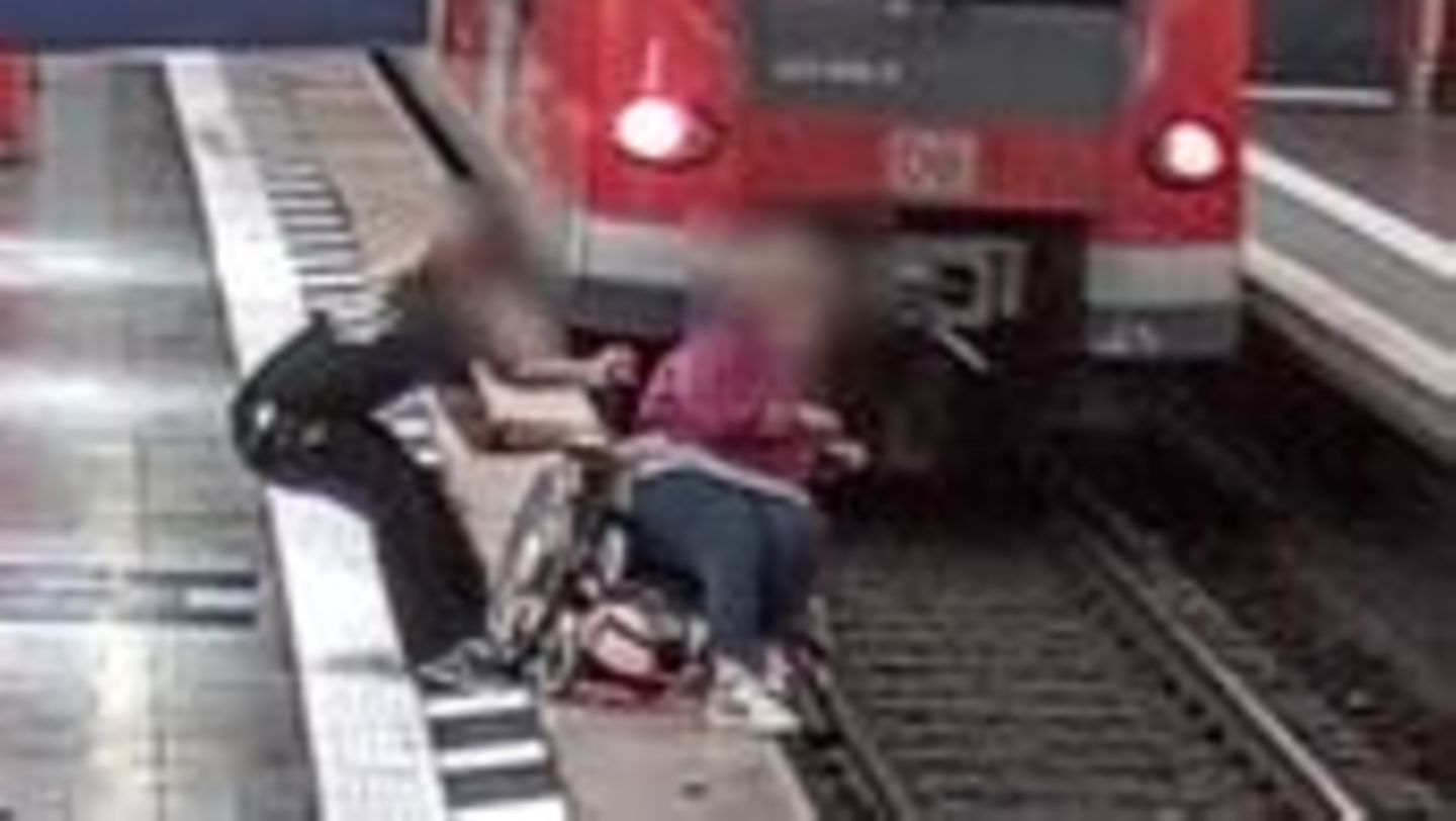 Ein Mann hält eine Rollstuhlfahrerin fest, um den Absturz ins Gleisbett zu verhindern