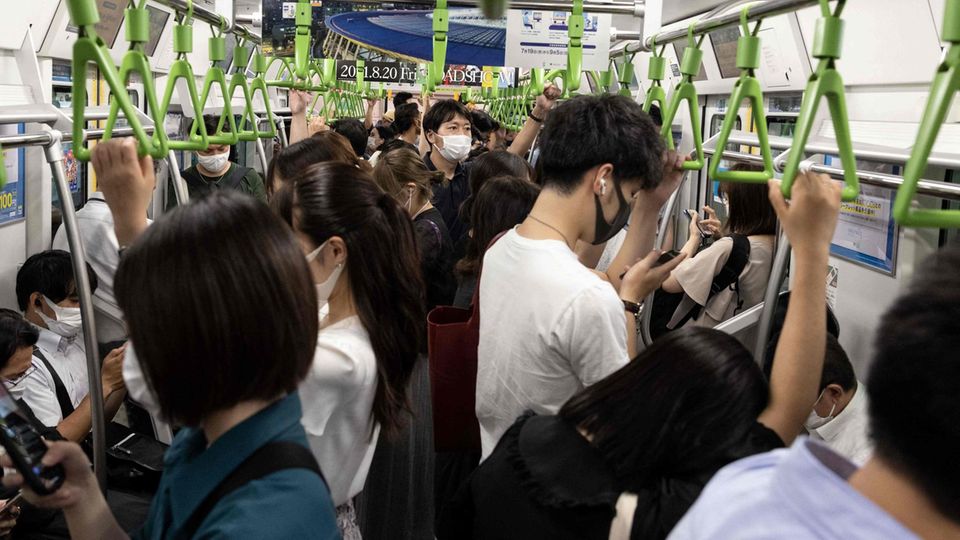 In einem vollen Waggon stehen Japanerinnen und Japaner dicht an dicht und halten sich an grünen, dreieckigen Haltegriffen fest