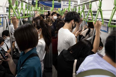 In einem vollen Waggon stehen Japanerinnen und Japaner dicht an dicht und halten sich an grünen, dreieckigen Haltegriffen fest