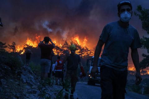Einsatzkräfte gehen nach einem Einsatz in der Nähe des Dorfes Akcayaka, während im Hintergrund das Feuer eines Waldbrandes wütet