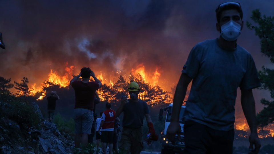 Einsatzkräfte gehen nach einem Einsatz in der Nähe des Dorfes Akcayaka, während im Hintergrund das Feuer eines Waldbrandes wütet