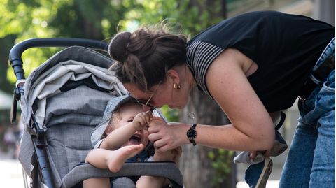 Eine Frau beugt sich zu ihrem Kind im Kinderwagen und lacht