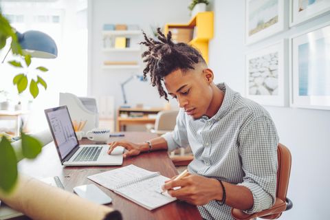 Laptop für Studenten: Ein Student sitzt am Laptop, notiert aber etwas per Hand auf seinem Block.