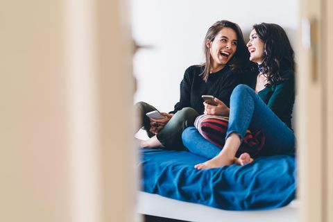Zwei Freundinnen sitzen gemeinsam auf dem Bett und lachen