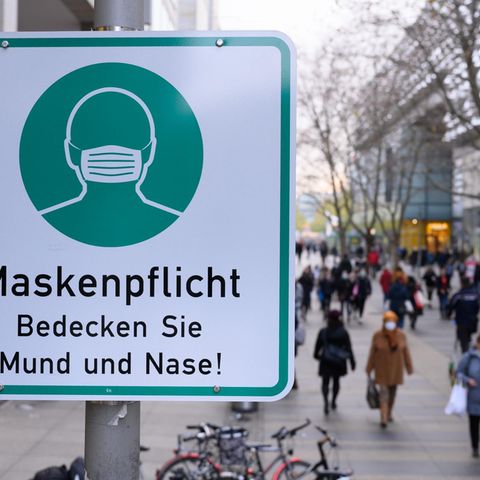 Ein Hinweisschild auf die Maskenpflicht hängt auf der Einkaufsstraße Prager Straße an einem Lampenmas