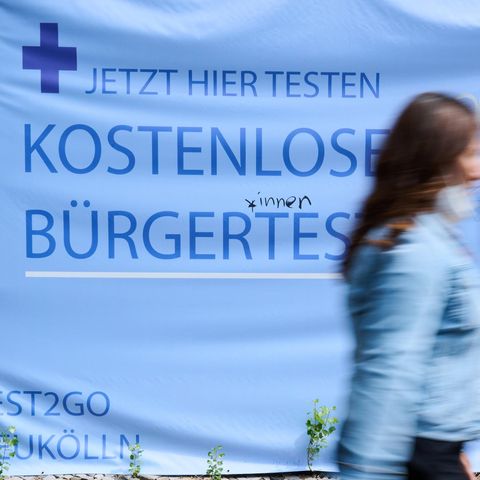 Menschen gehen vor einem Hinweisschild auf kostenlose Bürgertests entlang
