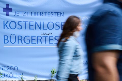 Menschen gehen vor einem Hinweisschild auf kostenlose Bürgertests entlang