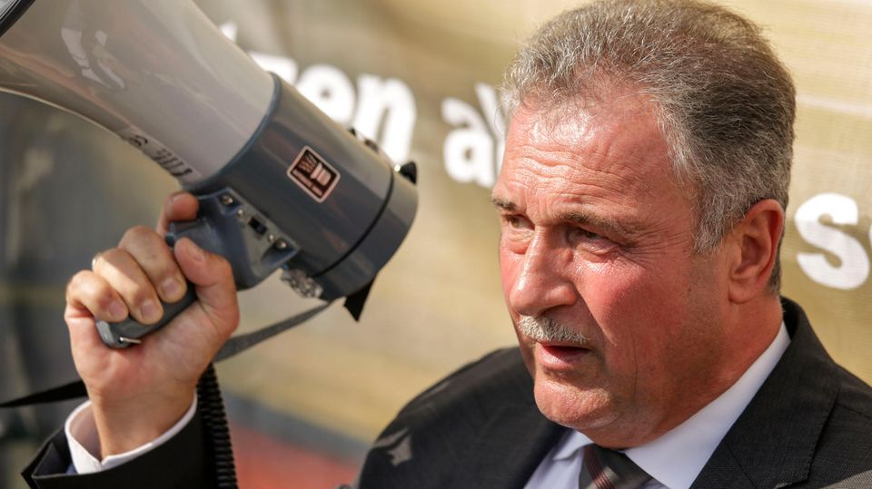 Claus Weselsky GDL Ein weißer Mann in Anzug und Krawatte steht im Sonnenschein, während er in ein Megafon spricht. Er hat einen graue Haare