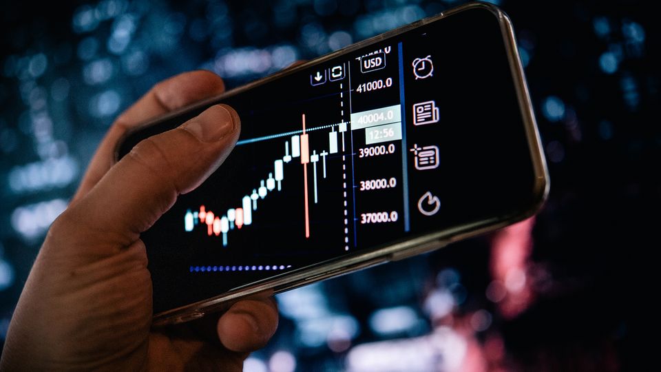 Inflation: Ein Smartphone-Display zeigt schwankende Aktienkurse