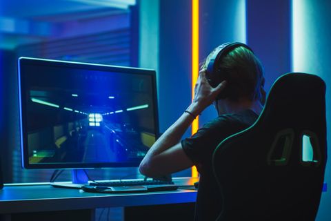 Ein Zocker sitzt vor seinem 144-Hz-4K-Monitor und setzt sich ein Headset auf.