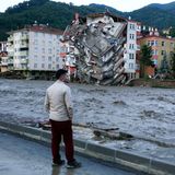 Ein Mann steht auf einem asphaltierten Flussufer, während kurz vor seinen Füßen Wassermassen vorbeiströmen