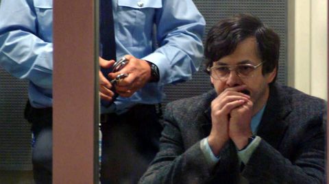 Ein bieder wirkender Mann mit schwarzem Seitenscheitel und silberner Brille sitzt mit Händen vor dem Mund vor Gericht